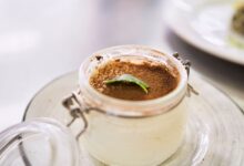 Close-up of creamy tiramisu dessert in a jar, topped with cocoa and mint leaf.