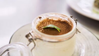 Close-up of creamy tiramisu dessert in a jar, topped with cocoa and mint leaf.