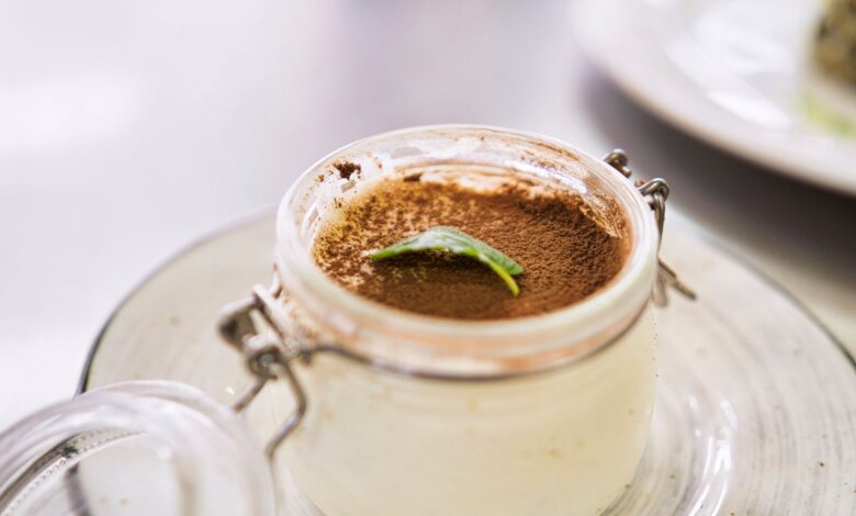 Close-up of creamy tiramisu dessert in a jar, topped with cocoa and mint leaf.