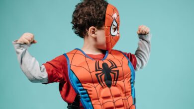 Young child posing in Spider-Man costume with turquoise background showcasing imagination.