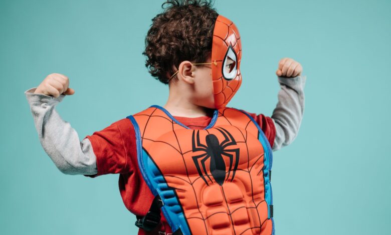 Young child posing in Spider-Man costume with turquoise background showcasing imagination.