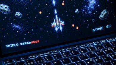 A classic arcade space shooter game displayed on a laptop with illuminated keyboard, showing retro graphics.