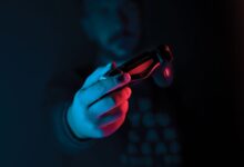 Close-up of a man's hand holding a joystick against a dark background with red and blue lighting.