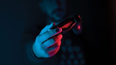 Close-up of a man's hand holding a joystick against a dark background with red and blue lighting.