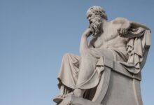 Stone statue of philosopher Socrates sitting in thoughtful pose in Athens, Greece under a clear blue sky.