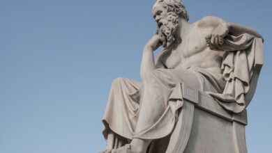 Stone statue of philosopher Socrates sitting in thoughtful pose in Athens, Greece under a clear blue sky.