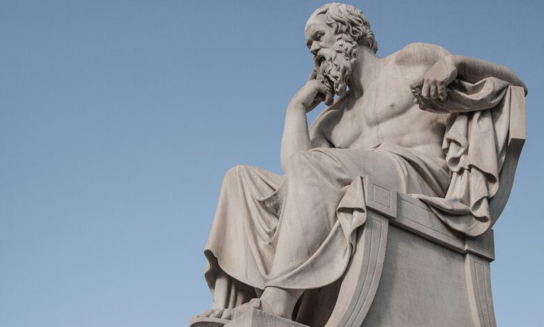 Stone statue of philosopher Socrates sitting in thoughtful pose in Athens, Greece under a clear blue sky.