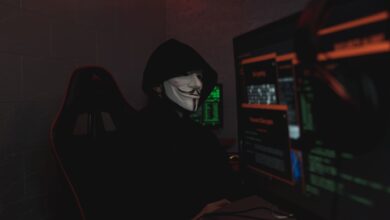 An anonymous hacker wearing a mask working on a computer in a dark room.
