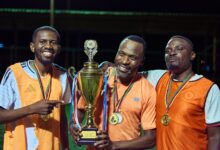 Three soccer players celebrating with medals and a trophy at night.