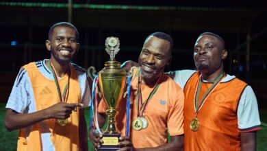 Three soccer players celebrating with medals and a trophy at night.