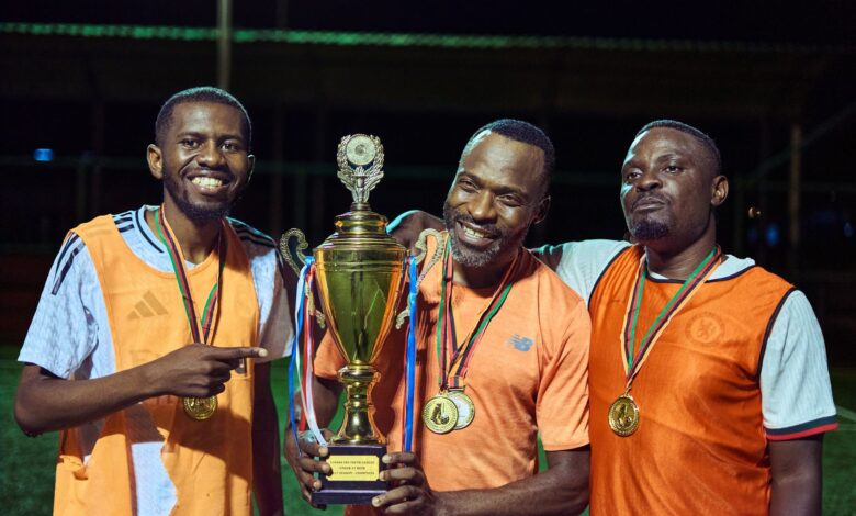 Three soccer players celebrating with medals and a trophy at night.