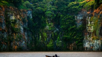 Ancient sculptures carved into a cliffside, reflected in the serene river below.