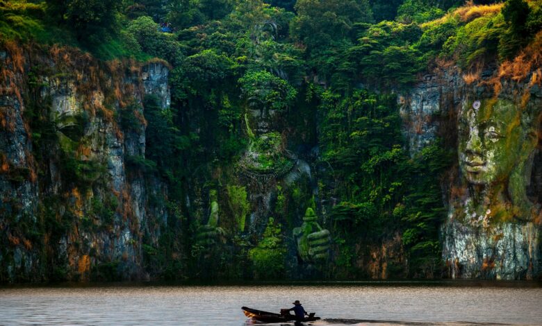 Ancient sculptures carved into a cliffside, reflected in the serene river below.