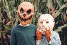 Two children wearing Halloween masks stand in a cornfield, creating a spooky scene.