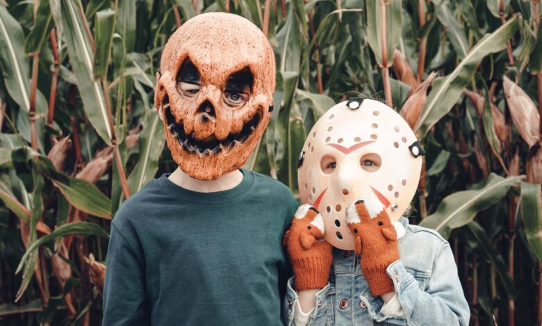 Two children wearing Halloween masks stand in a cornfield, creating a spooky scene.