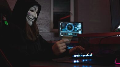 Masked hacker with credit card at computer, symbolizing cybercrime and anonymity.
