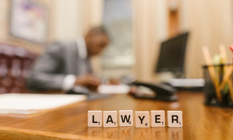 Wooden letter tiles spelling 'LAWYER' on a desk, with blurred office setting in the background.