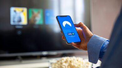 Person using VPN on smartphone while watching smart TV at home.