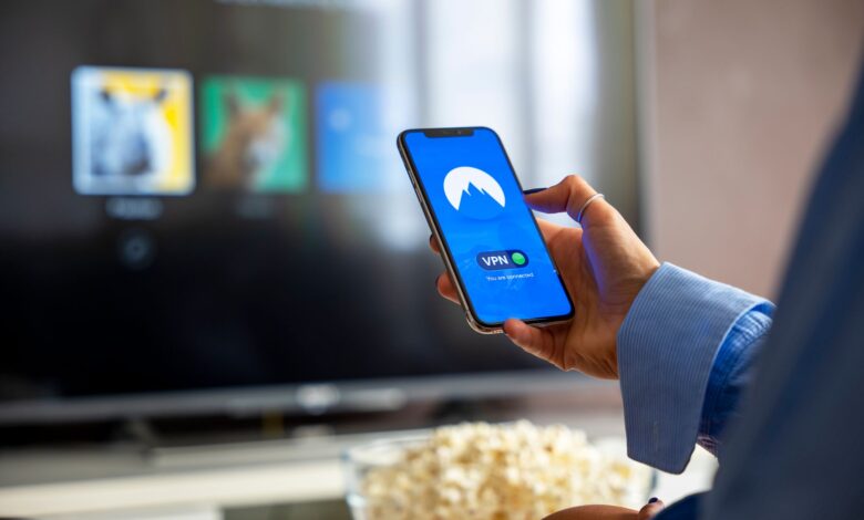 Person using VPN on smartphone while watching smart TV at home.