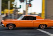 A classic orange car driving quickly through city streets, capturing motion and nostalgia.