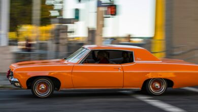 A classic orange car driving quickly through city streets, capturing motion and nostalgia.