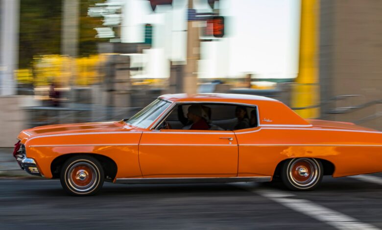 A classic orange car driving quickly through city streets, capturing motion and nostalgia.