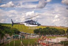 A helicopter gliding over lush fields with a vibrant blue sky backdrop.