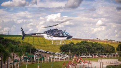 A helicopter gliding over lush fields with a vibrant blue sky backdrop.