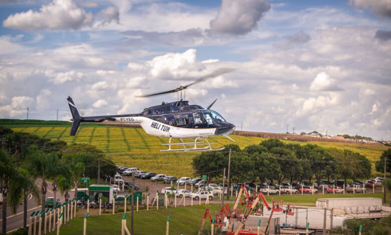 A helicopter gliding over lush fields with a vibrant blue sky backdrop.
