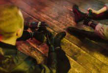 Two people with prosthetic hands playing video games on a wooden floor.