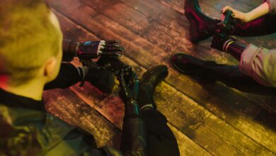 Two people with prosthetic hands playing video games on a wooden floor.