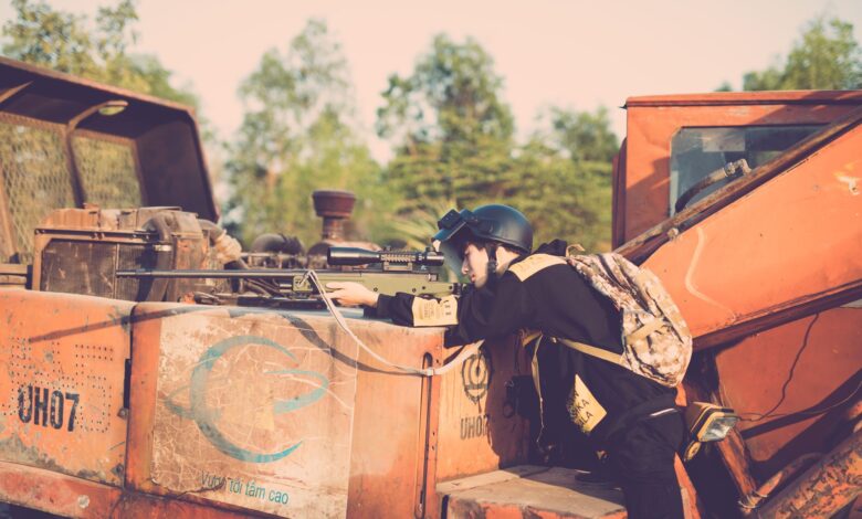 Person engaging in realistic outdoor play with a toy sniper rifle on industrial machinery.
