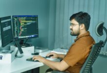 A focused developer coding at a modern office with dual monitors, showcasing a tech-driven workspace.