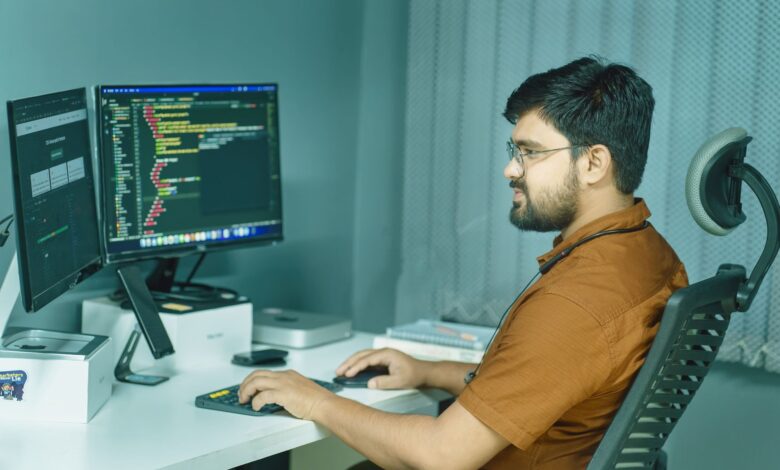 A focused developer coding at a modern office with dual monitors, showcasing a tech-driven workspace.