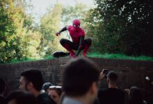 Spider-Man cosplayer posing for photos at an outdoor event, attracting a lively crowd.