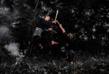 Two martial artists engaged in a high-flying sword fight in a dense forest.