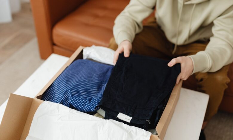 Man unboxing new clothes from a cardboard box on a table indoors.