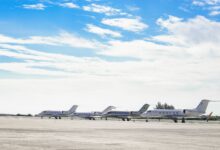 Row of private jets parked on a clear day at an open runway, showcasing aviation and luxury travel.