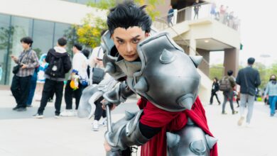 Man in intricate fantasy armor posing at a vibrant outdoor cosplay event.