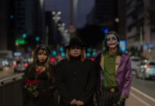 A trio in Halloween-themed cosplay walking through a bustling city street at night.