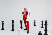 A person in red holding a large chess piece surrounded by giant chess pieces.