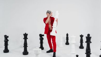 A person in red holding a large chess piece surrounded by giant chess pieces.