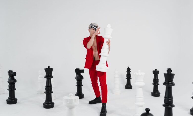 A person in red holding a large chess piece surrounded by giant chess pieces.