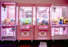 Rows of illuminated pink claw machines filled with vibrant soft toys indoors.