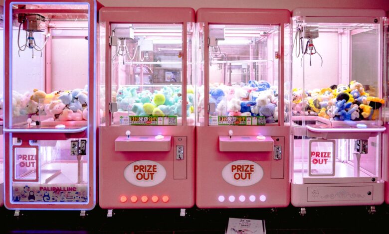 Rows of illuminated pink claw machines filled with vibrant soft toys indoors.