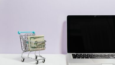 Mini shopping cart with cash beside a laptop, symbolizing online shopping and e-commerce.