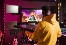 A man in a yellow jacket playing Guitar Hero on a monitor indoors, enjoying e-sports.