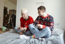 Two men in festive sweaters playing video games and enjoying each other's company at home.