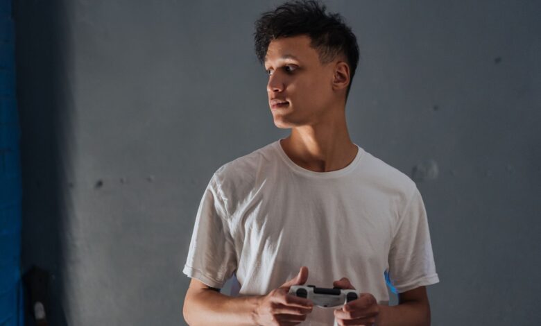 A young man wearing a white t-shirt focuses intently while holding a game controller indoors.