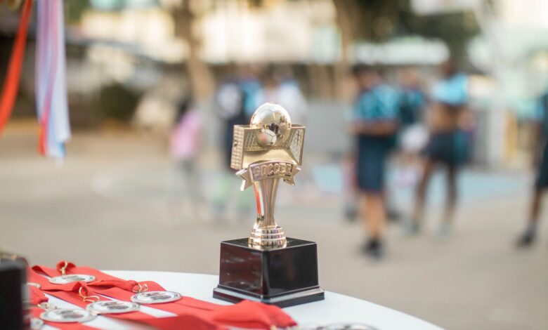 Close-up of a polished soccer trophy with medals at an outdoor sports award ceremony.